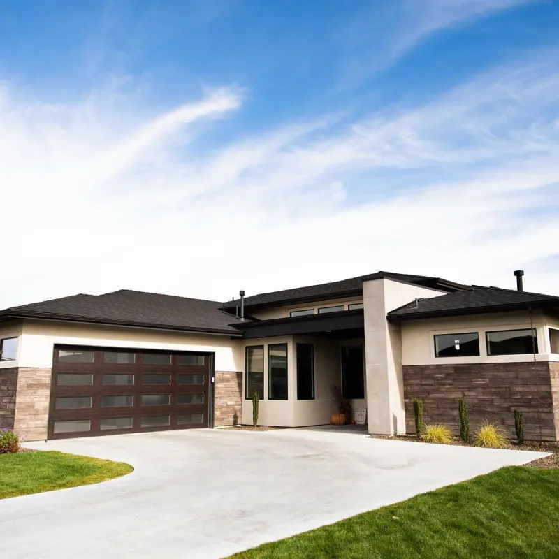 White modern garage door with vertical glass panels on dark stone wall