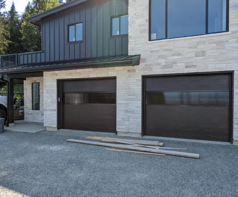 Modern dark flush garage doors with tinted glass panels on stone facade