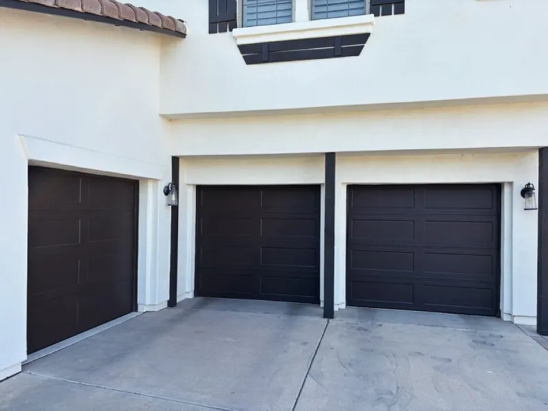 Three dark flush panel garage doors on stucco home
